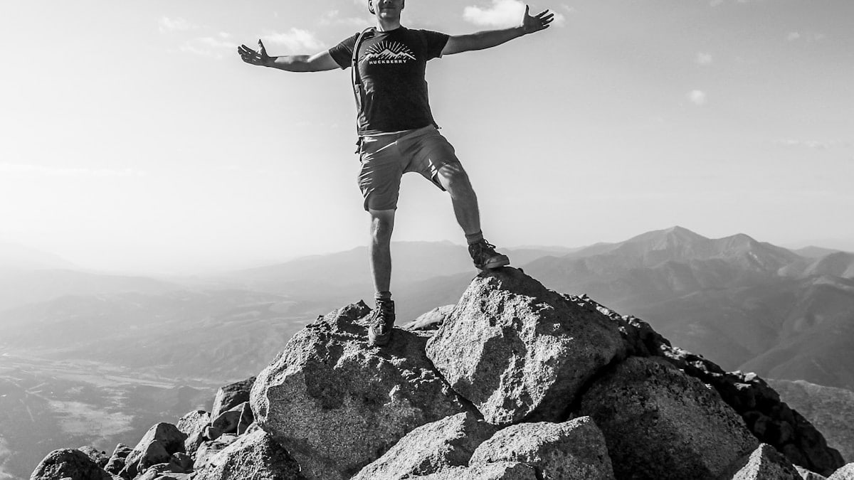 man in black tank top and white shorts standing on rock formation during daytime
